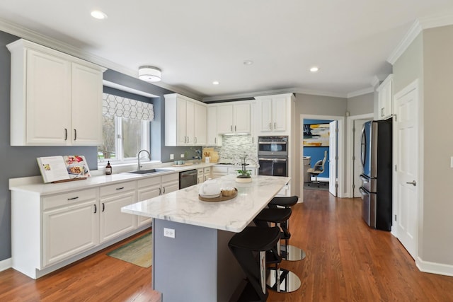 kitchen with white cabinetry, stainless steel appliances, a kitchen breakfast bar, and a sink