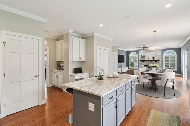kitchen with gray cabinetry, a kitchen island, open floor plan, ornamental molding, and wood finished floors