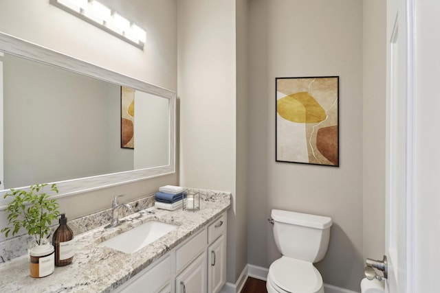 half bathroom featuring toilet, vanity, and baseboards