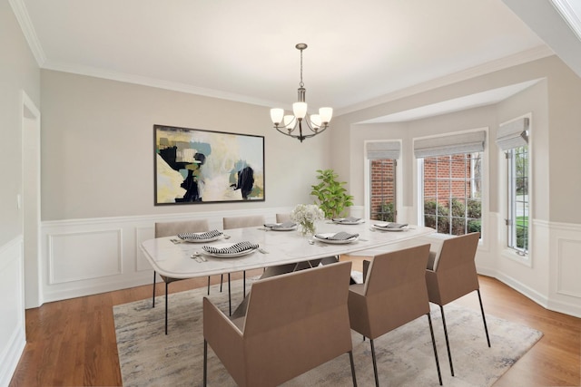 dining space featuring an inviting chandelier, crown molding, a wainscoted wall, a decorative wall, and wood finished floors