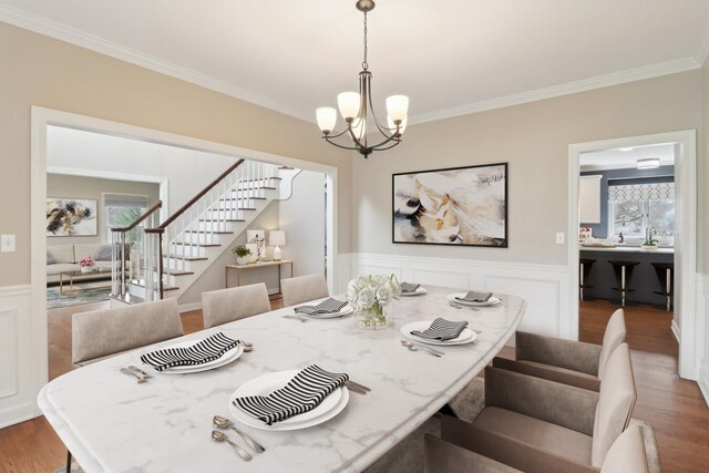 dining room with stairway, a chandelier, crown molding, wainscoting, and wood finished floors
