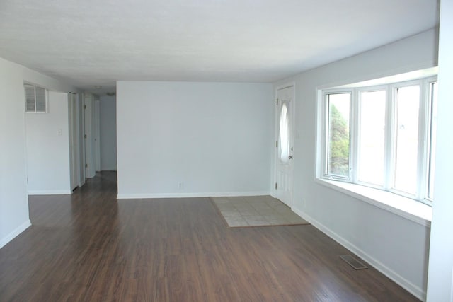 unfurnished living room featuring dark wood finished floors, visible vents, and baseboards