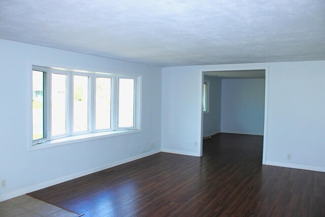 spare room with baseboards, a textured ceiling, and dark wood-type flooring