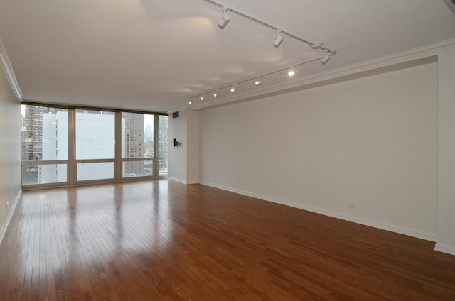 empty room with baseboards, rail lighting, ornamental molding, and wood finished floors