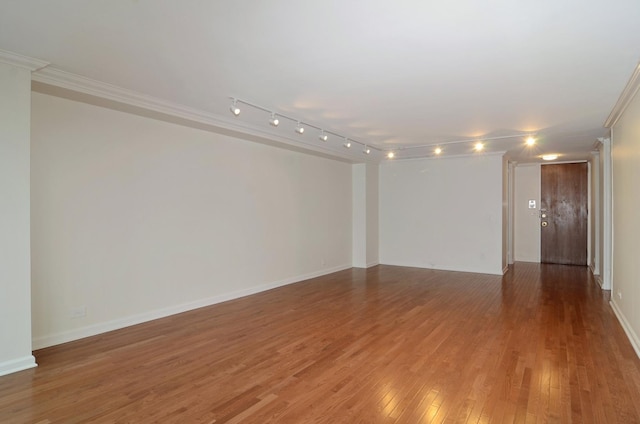 empty room featuring crown molding, baseboards, track lighting, and light wood-style floors