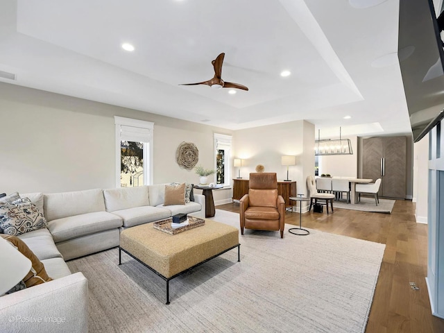 living room featuring recessed lighting, a raised ceiling, wood finished floors, and ceiling fan with notable chandelier