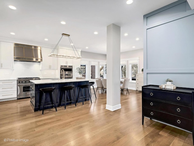 kitchen featuring a kitchen breakfast bar, exhaust hood, light countertops, appliances with stainless steel finishes, and white cabinetry