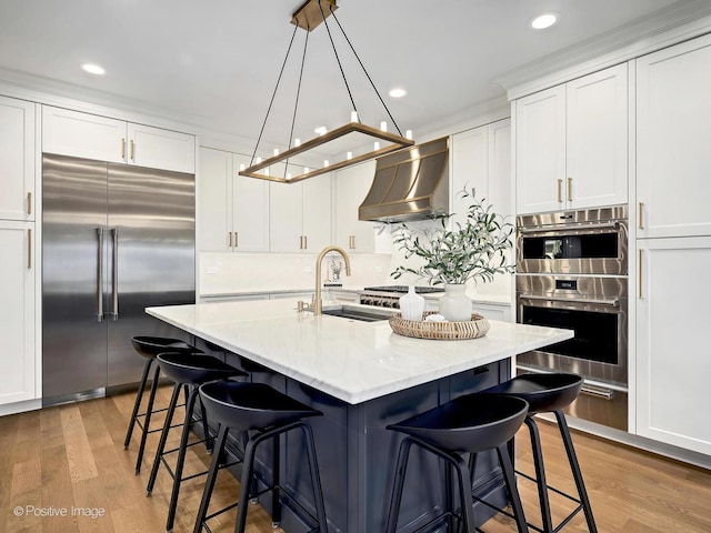 kitchen with wall chimney range hood, appliances with stainless steel finishes, a sink, and white cabinetry