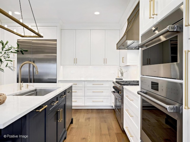 kitchen with premium appliances, a sink, light countertops, wall chimney exhaust hood, and white cabinetry