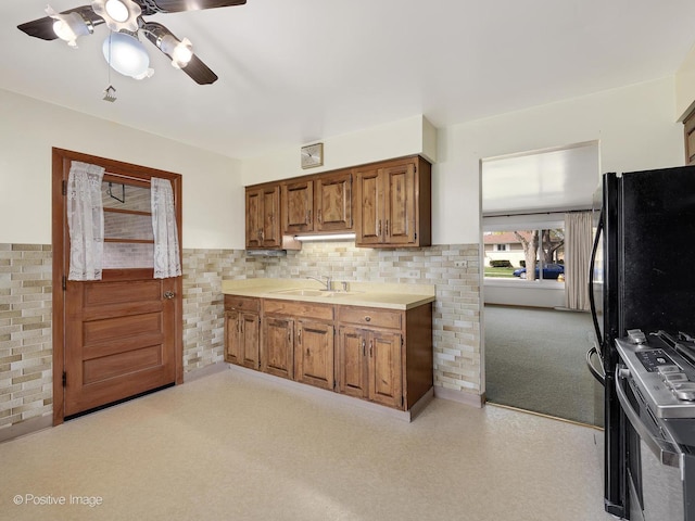 kitchen with ceiling fan, brown cabinetry, a sink, light countertops, and stainless steel range oven