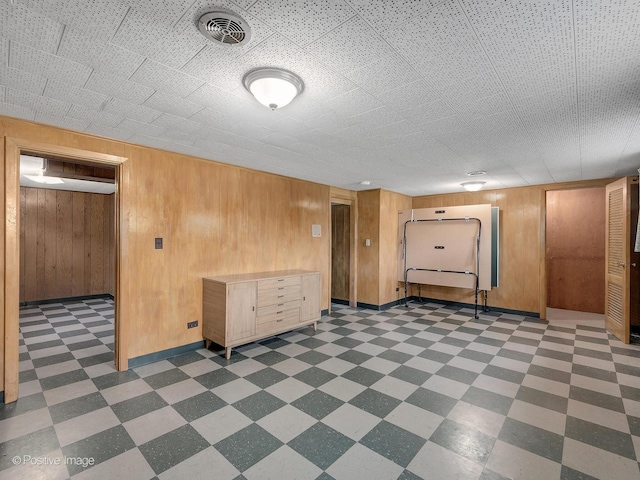 finished below grade area featuring visible vents, wood walls, and tile patterned floors