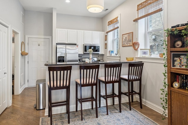 kitchen with appliances with stainless steel finishes, a kitchen bar, dark countertops, wood finished floors, and white cabinetry