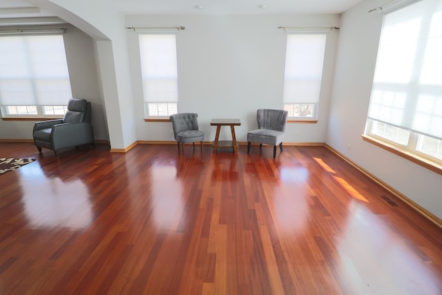 living area with arched walkways, baseboards, wood finished floors, and visible vents