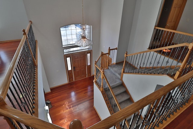 foyer entrance with baseboards, a high ceiling, a notable chandelier, and wood finished floors