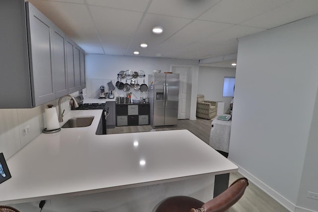 kitchen with appliances with stainless steel finishes, a sink, light countertops, a paneled ceiling, and a kitchen bar