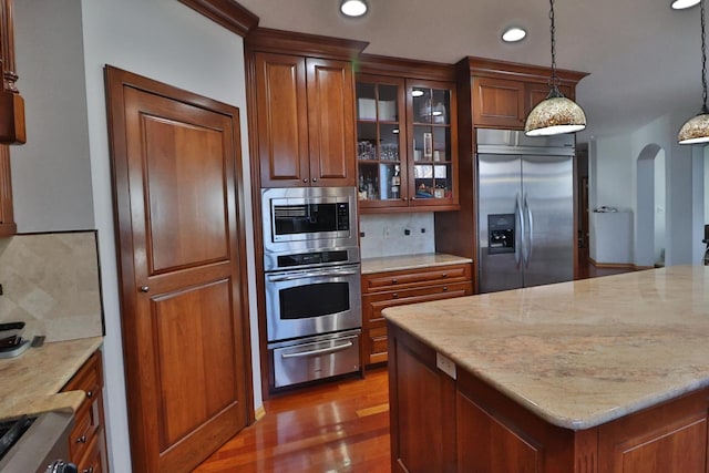 kitchen with a warming drawer, arched walkways, tasteful backsplash, wood finished floors, and built in appliances