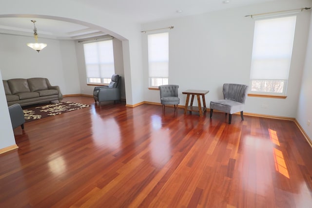 living area with arched walkways, baseboards, and wood finished floors