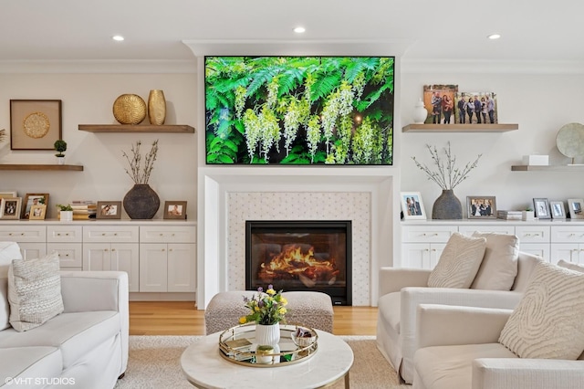 living area with crown molding, light wood-style flooring, recessed lighting, and a glass covered fireplace