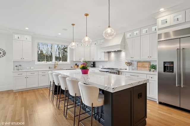 kitchen featuring built in fridge, custom exhaust hood, light wood finished floors, a sink, and a center island