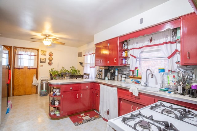kitchen with red cabinetry, a ceiling fan, a sink, stainless steel refrigerator, and white range with gas cooktop