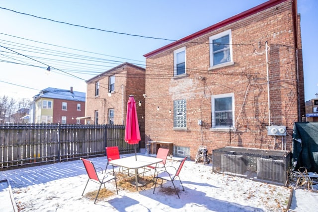 snow covered house featuring brick siding, a patio area, and fence