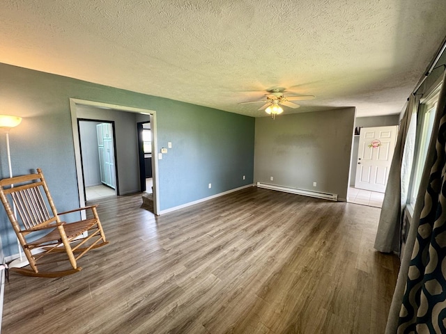 26812 US-150 Hwy, Leroy, IL 61752 - unfurnished living room featuring a baseboard radiator, wood finished floors, a textured ceiling, ceiling fan, and baseboards