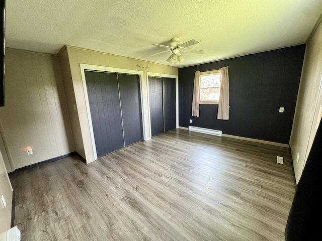 26812 US-150 Hwy, Leroy, IL 61752 - unfurnished bedroom with baseboard heating, multiple closets, wood finished floors, a textured ceiling, and ceiling fan