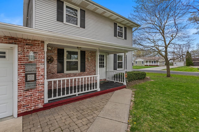 entrance to property with brick siding, a lawn, and covered porch