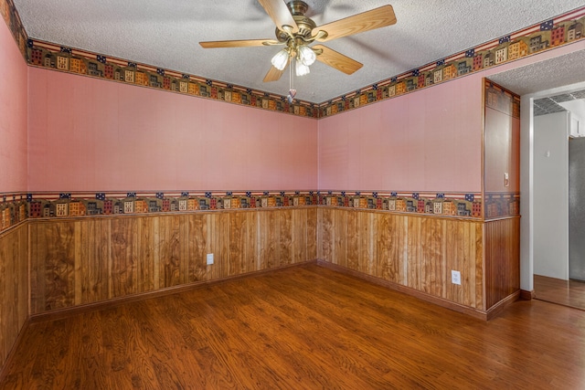 unfurnished room featuring wooden walls, wood finished floors, a textured ceiling, and a ceiling fan