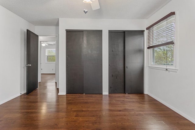 unfurnished bedroom featuring a ceiling fan, wood finished floors, a textured ceiling, multiple closets, and baseboards