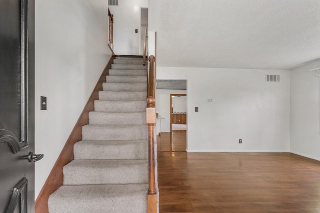 stairway with baseboards, wood finished floors, visible vents, and a textured ceiling