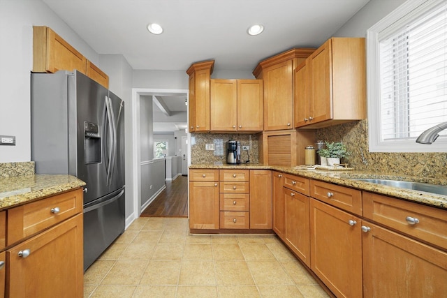 kitchen featuring stainless steel fridge with ice dispenser, recessed lighting, tasteful backsplash, light stone counters, and a sink