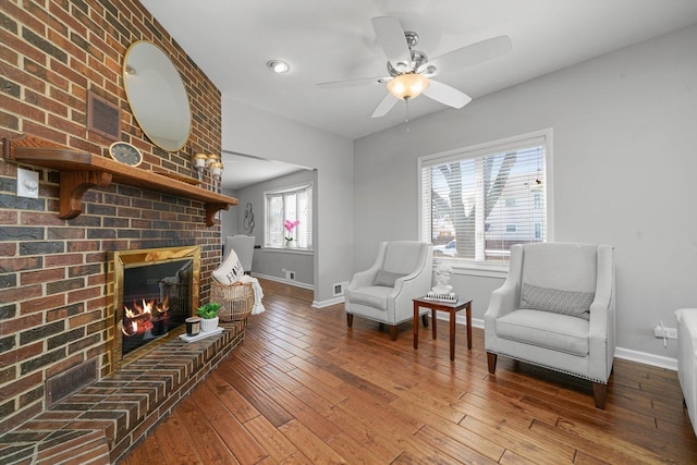 sitting room featuring baseboards, ceiling fan, a brick fireplace, and hardwood / wood-style flooring