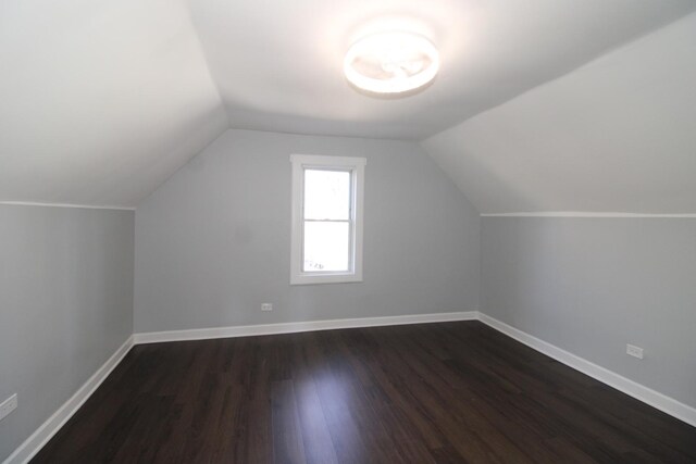 additional living space featuring dark wood finished floors, lofted ceiling, and baseboards