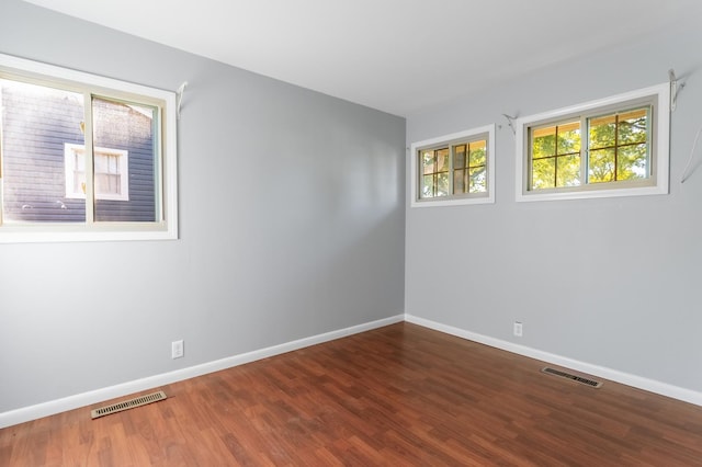 spare room featuring wood finished floors, visible vents, and baseboards