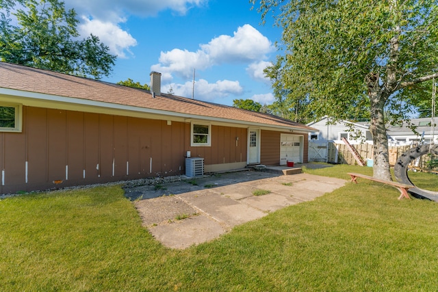 rear view of property with board and batten siding, a yard, a garage, and fence