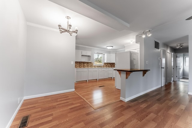 kitchen with a notable chandelier, a breakfast bar, visible vents, crown molding, and white cabinetry