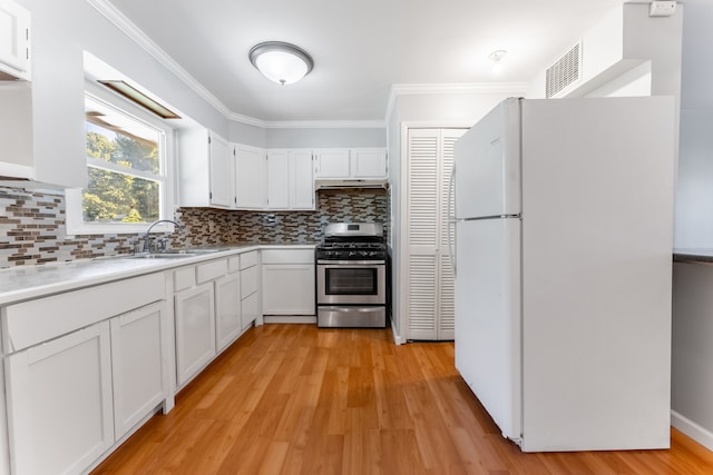 kitchen with crown molding, a sink, stainless steel gas stove, backsplash, and freestanding refrigerator