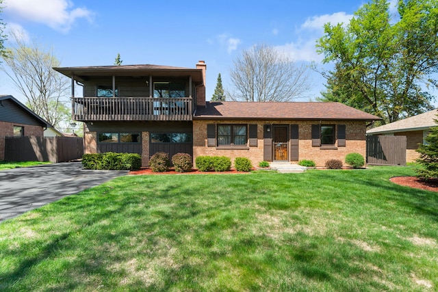 split level home with brick siding, a front lawn, fence, and a chimney