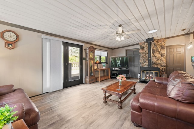 living area with ceiling fan, a wood stove, and light wood-style flooring