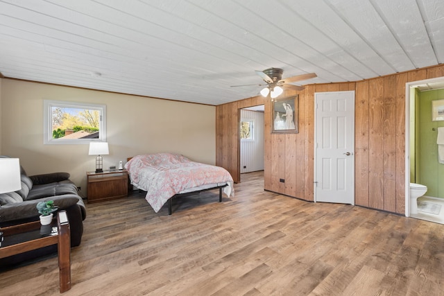 bedroom with wooden walls, a ceiling fan, light wood-style flooring, and ensuite bathroom