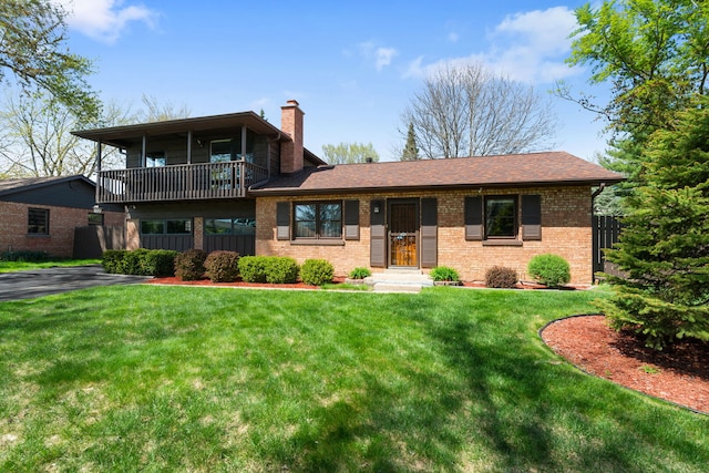 view of front of home featuring fence, a balcony, a front yard, a chimney, and brick siding