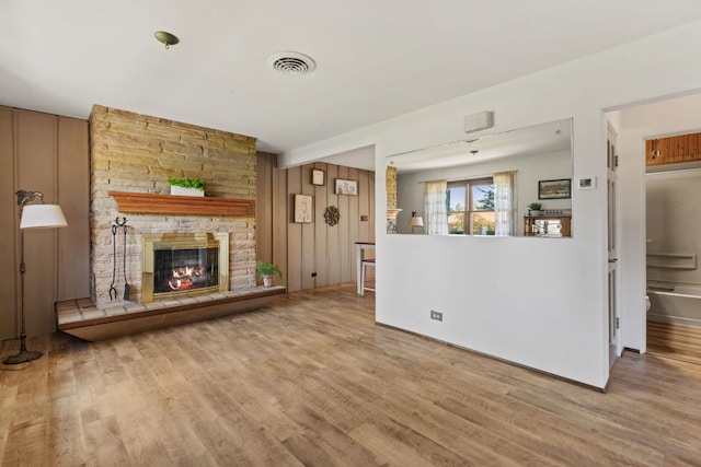 unfurnished living room with a stone fireplace, wood finished floors, and visible vents