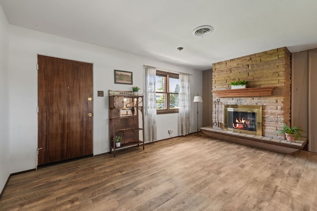 unfurnished living room with a stone fireplace, wood finished floors, and visible vents