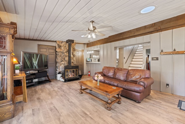 living area featuring wooden walls, ceiling fan, a wood stove, light wood-style floors, and stairway