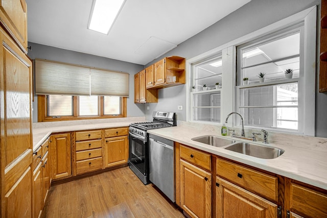 kitchen with appliances with stainless steel finishes, a sink, light countertops, and light wood-style flooring