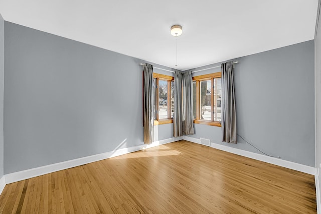 spare room with wood finished floors, visible vents, and baseboards