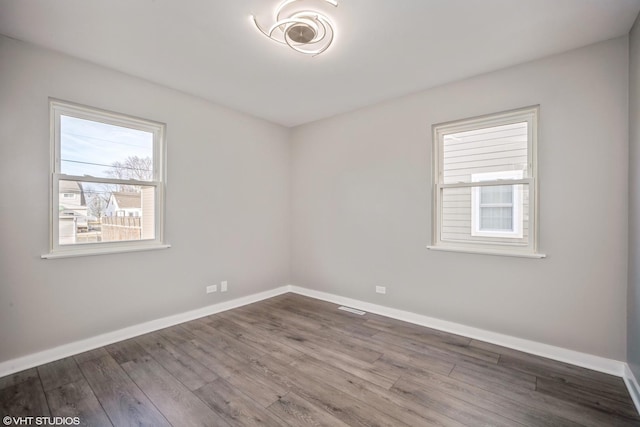 empty room with wood finished floors, visible vents, and baseboards