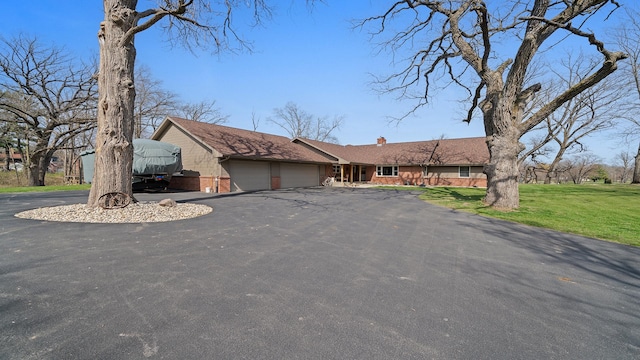 ranch-style house featuring a chimney, a front lawn, driveway, and a garage