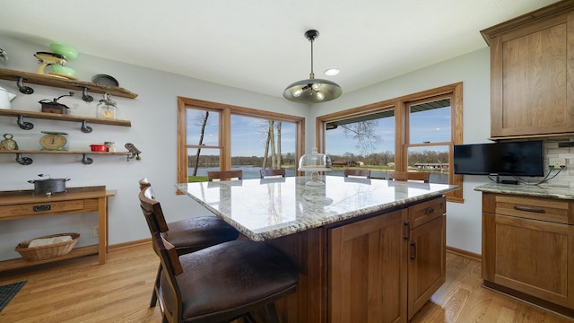 kitchen with a breakfast bar area, brown cabinets, light stone countertops, and light wood-type flooring